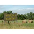 Bassett: This is a picture of the Bassett, NE sign, a strong ranching community, pictured is freshly baled hay.